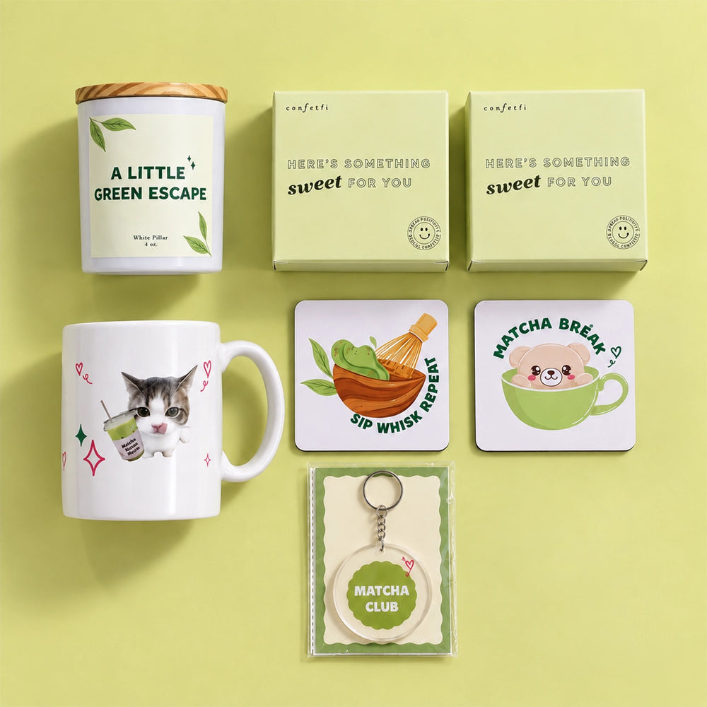 A curated collection of matcha-themed merchandise arranged on a pale yellow-green background, including a white canister labeled 'A LITTLE GREEN ESCAPE,' two pale green boxes reading 'HERE'S SOMETHING sweet for YOU,' a white mug with a cat and matcha drink illustration, a square coaster with a whisk and green leaves, a round matcha tea cup coaster with a bear, and a round keychain card reading 'MATCHA CLUB.'.